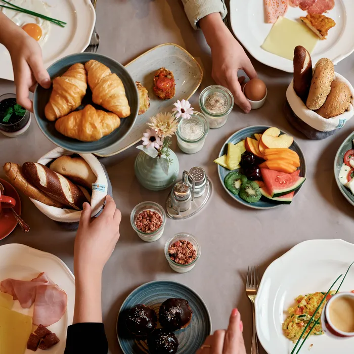 Tavola da brunch con croissant, frutta, formaggi, pane, uova, caffè e piatti da colazione assortiti